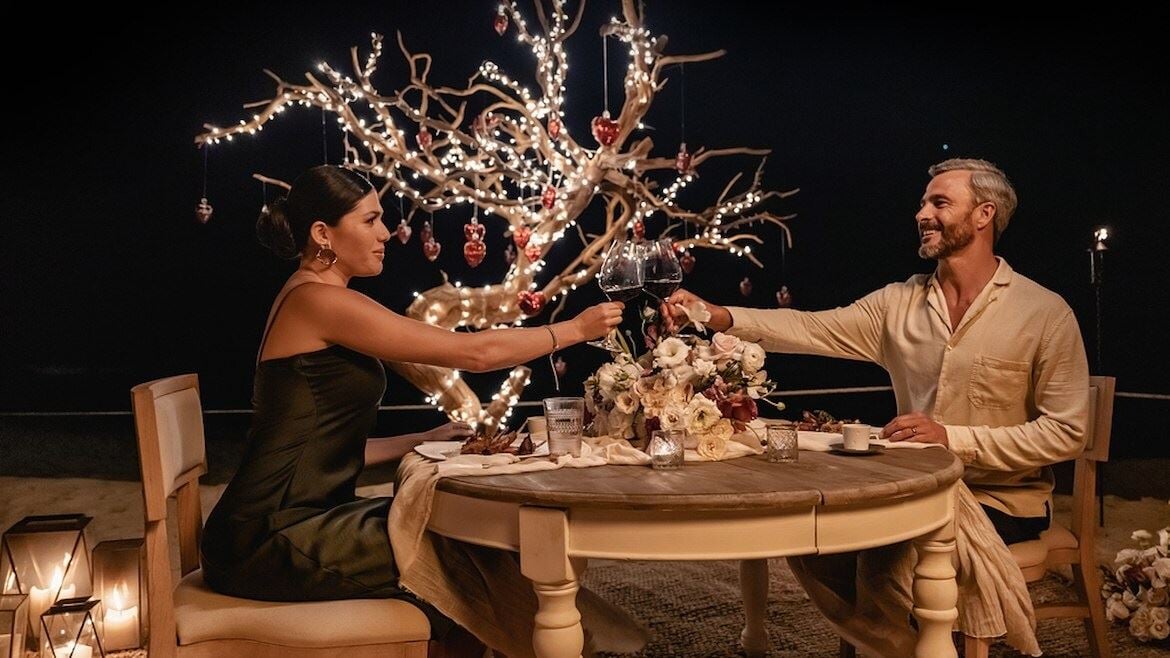 A man and woman sitting at a table with flowers and lights